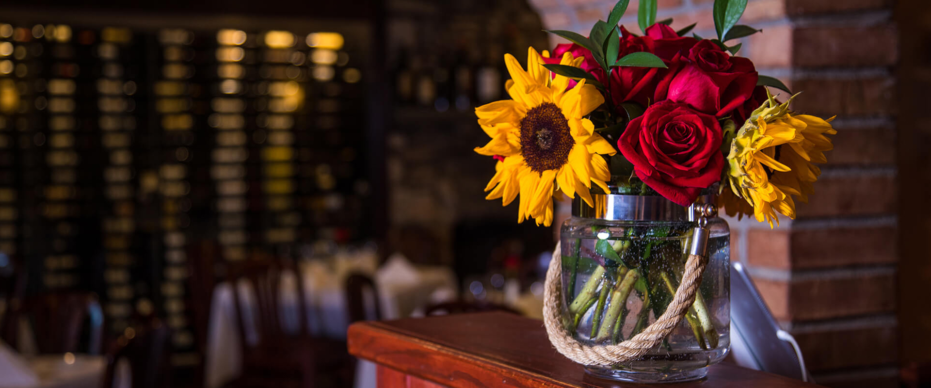 roses and sunflowers in a glass with wine racks in background
